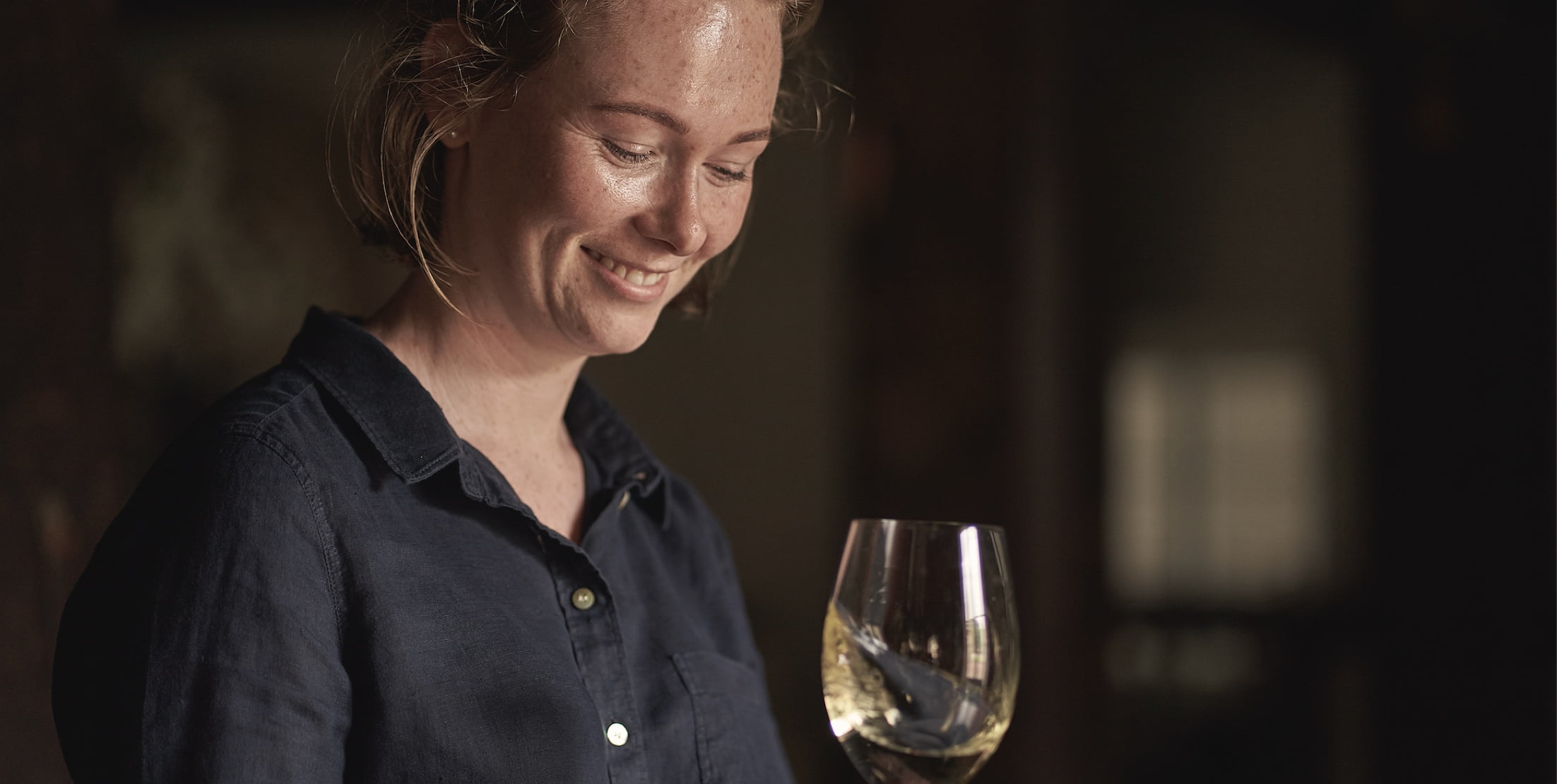 Young woman smiling and looking down at glass of white wine