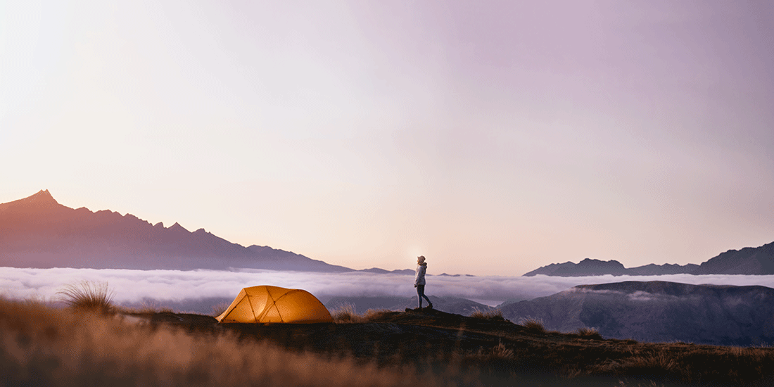 View of camping tent above the clouds on a mountainside with a person next to it