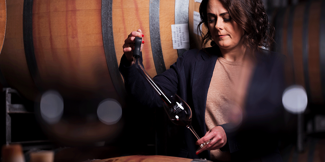 Dark haired woman taking wine from a large barrel via a wine tap