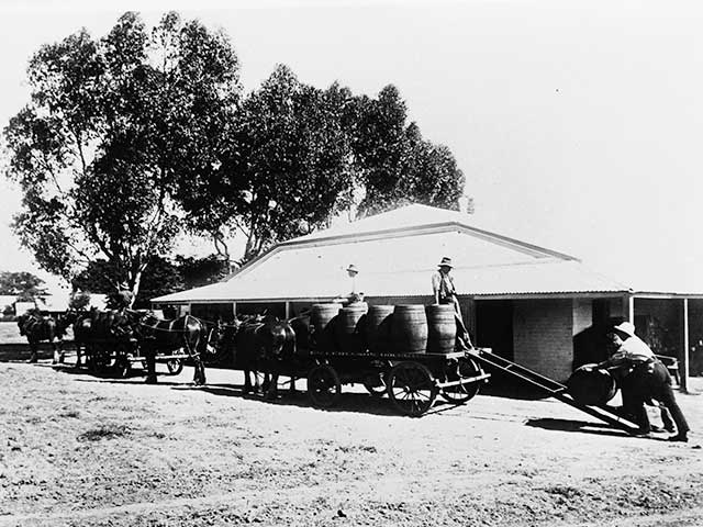 Black and white photograph of wine barrels being loaded on to a horse driven cart by two men