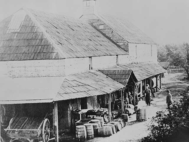 Black and white photograph of wine estate with barrels and workers outside