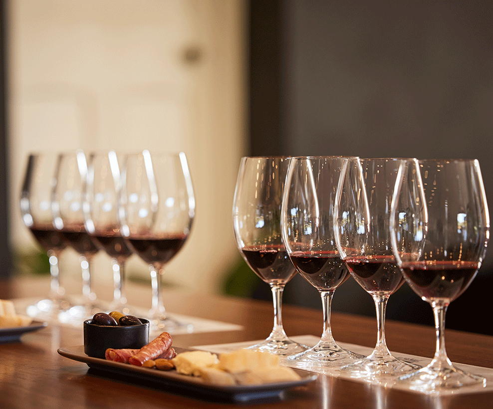 Two tasting trays of four red wines each on a table with a small cheeseboard in front of them