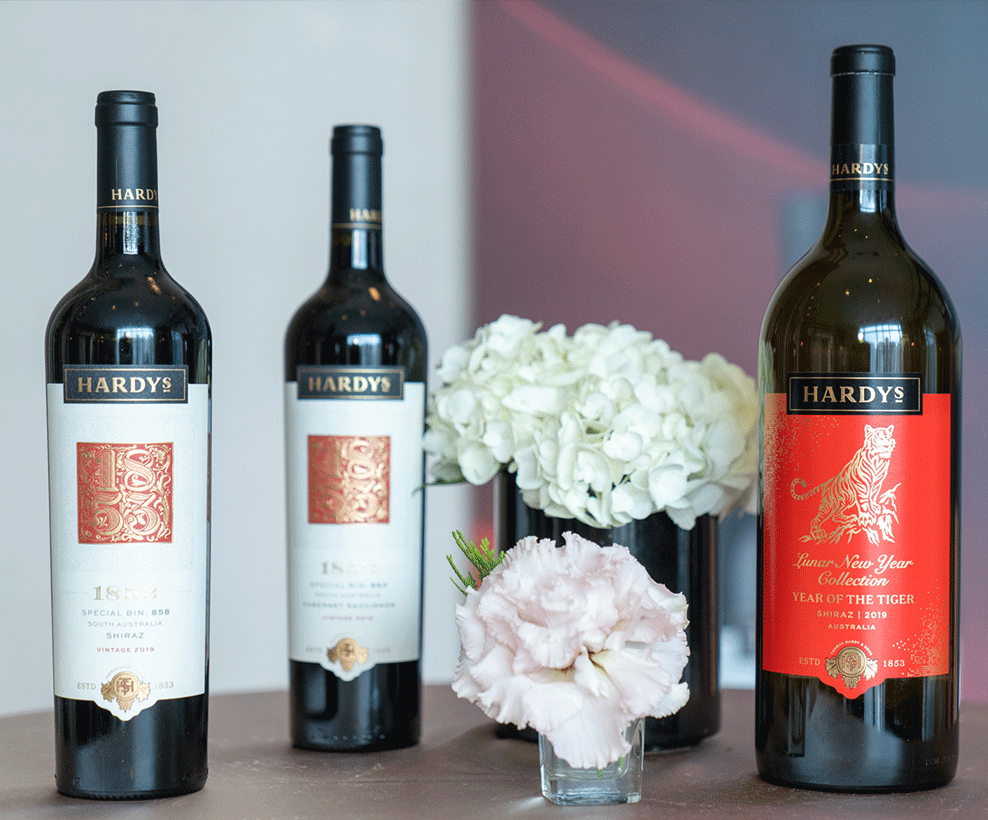 Three bottles of Hardys wines and two vases of flowers on a table