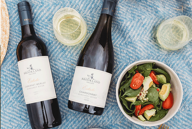 Flat lay shot of two bottles of Brookland Valley wine with two glasses and a small salad