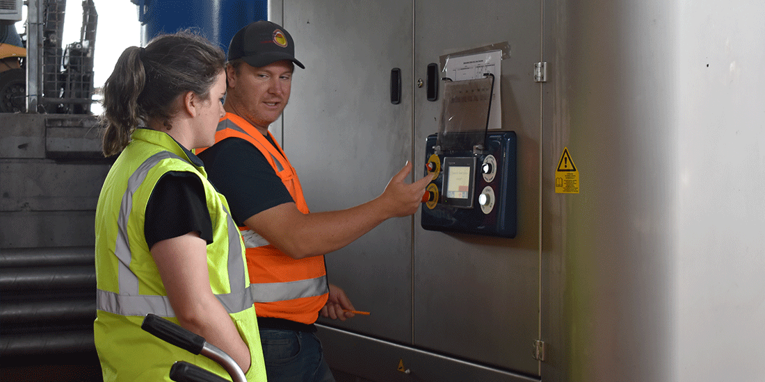 a man in orange high vis shows a woman in yellow high vis how to operate machinery