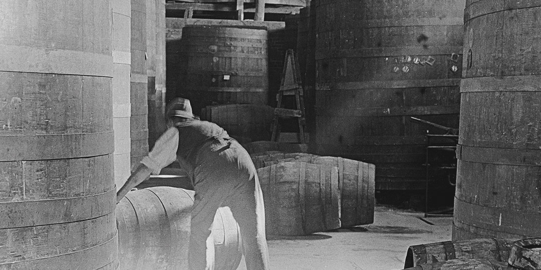 Old black and white photograph of man lifting barrel of wine