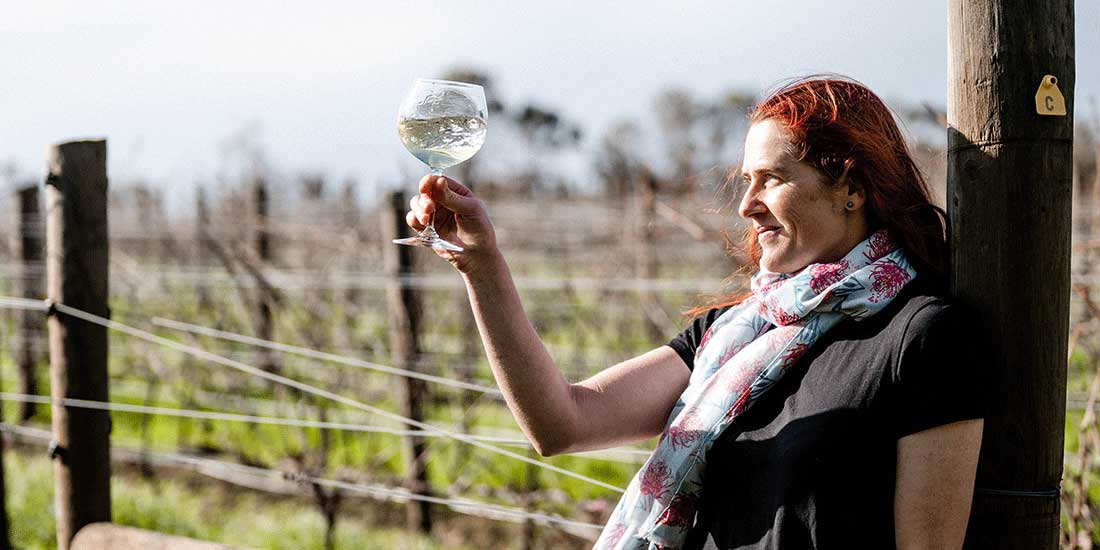 a winemaker observes a glass of white wine while standing in a vineyard