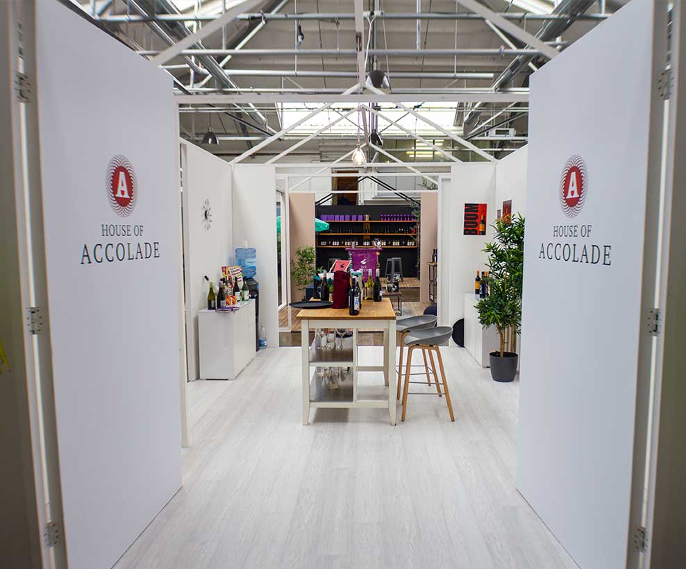 A white room with logos on doors that read House of Accolade leads into a room displaying wines